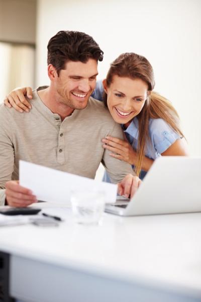 Couple smiling while looking at a laptop and holding paper
