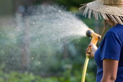 Woman in a hat spraying water from a hose
